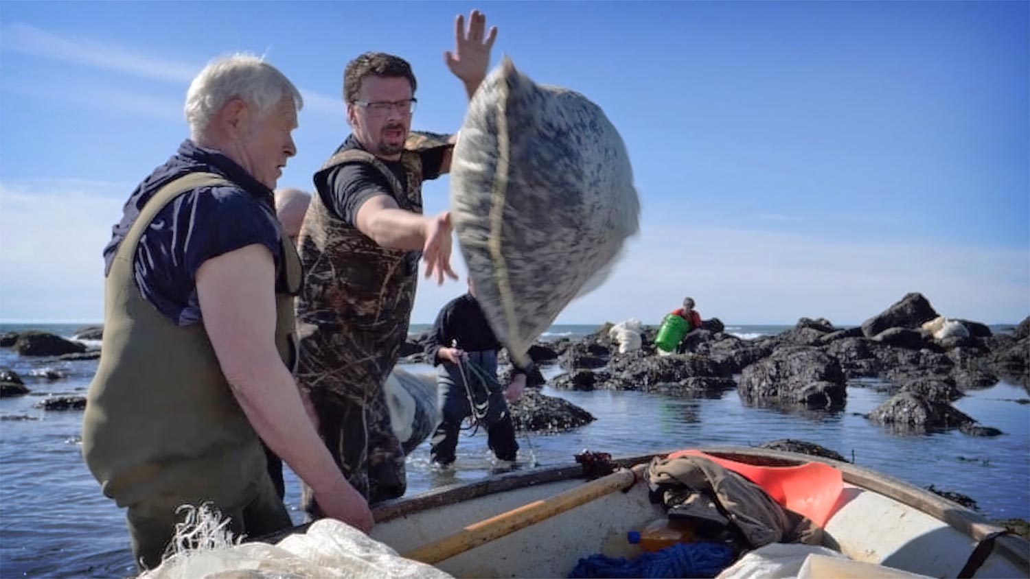 A man throwing a bag of dulse aboard a boat.