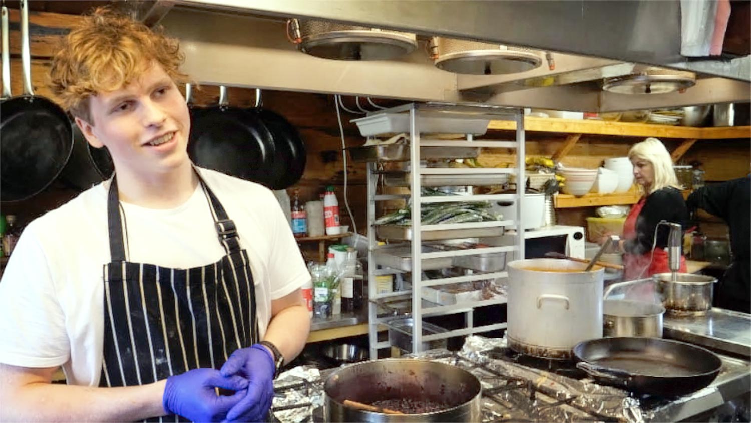 Young chef in the kitchen. His mother is in the background.