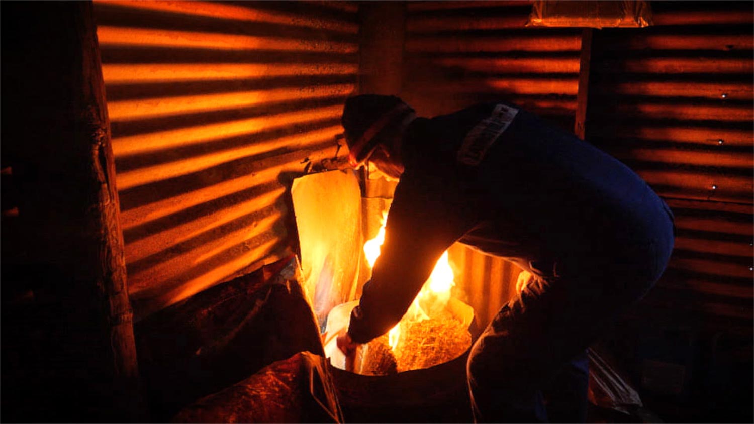 A man lighting fire in a shed for smoking fish and meat.