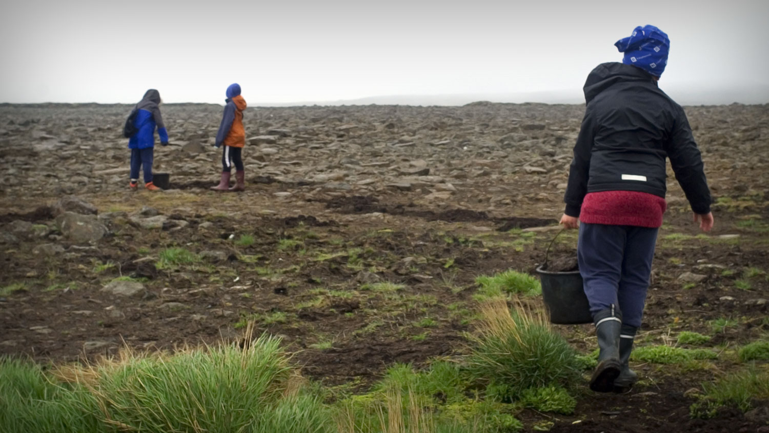 Three kids working on a stony field spreading fertilizer